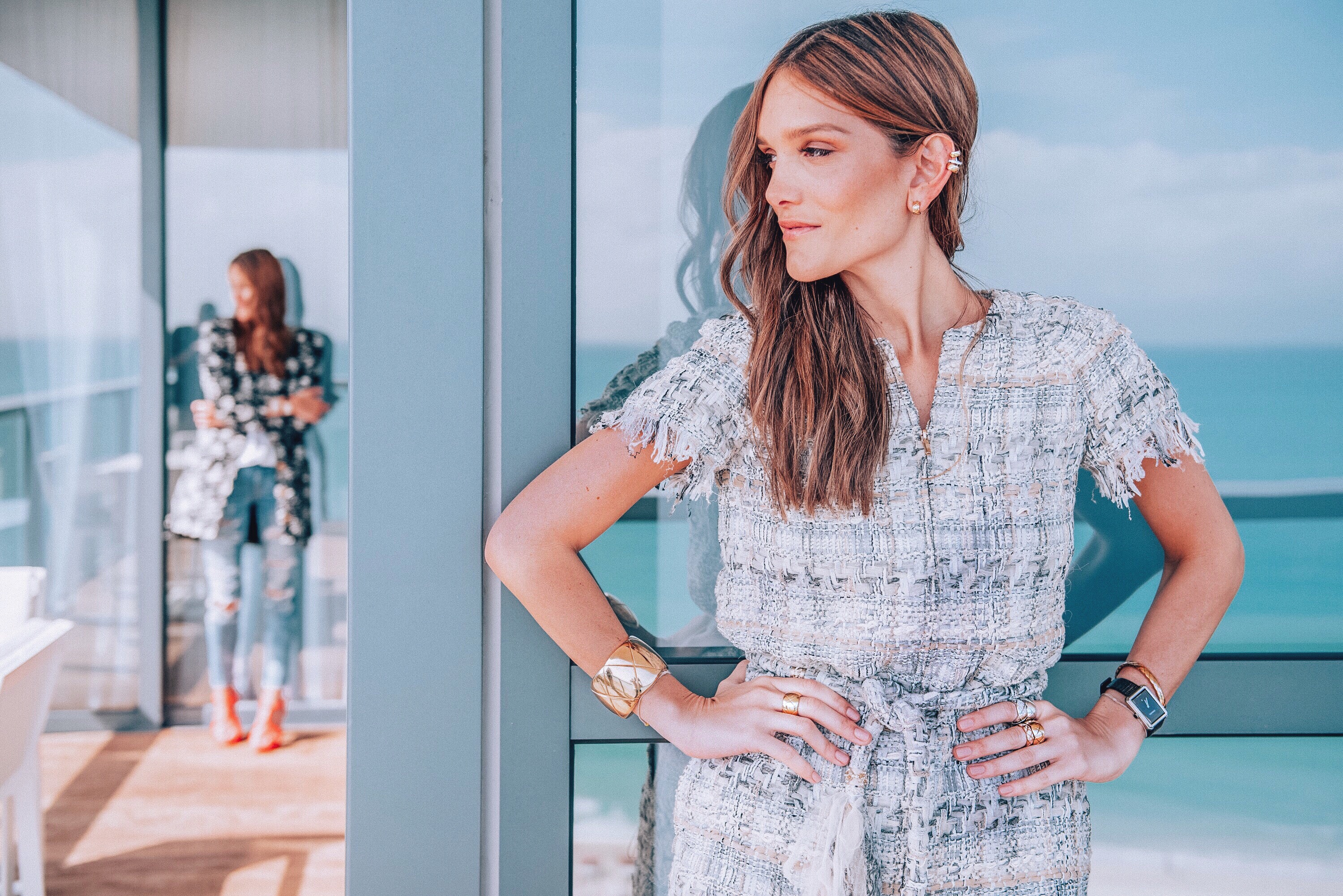 A woman in a silver textured dress poses beside a glass balcony overlooking the ocean