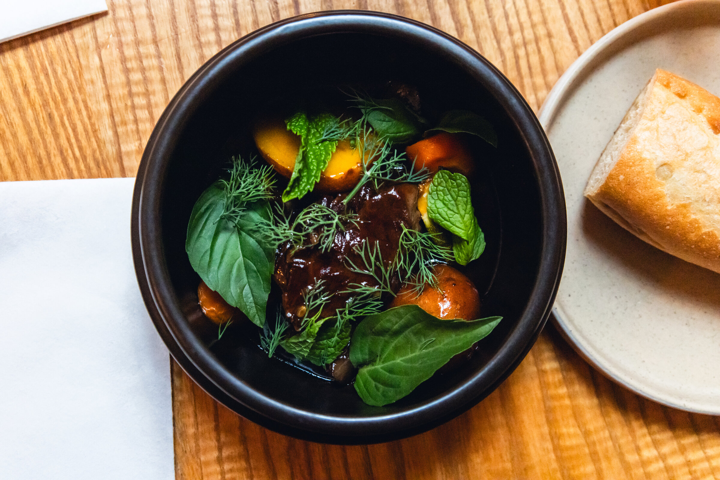 Overhead view of a composed dish with fresh herbs beside bread