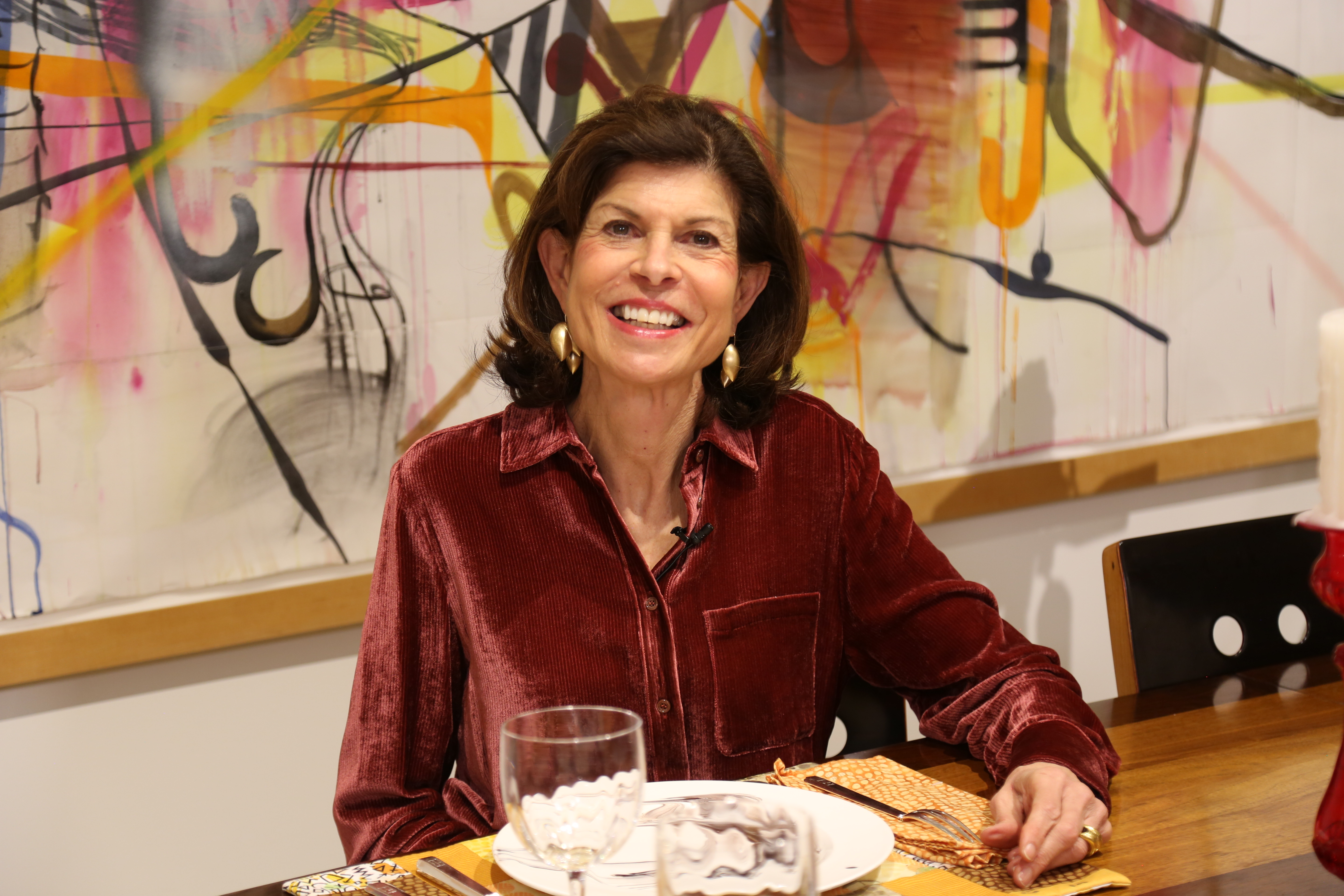 Gail Monaghan seated at a set dining table in front of a colorful abstract artwork