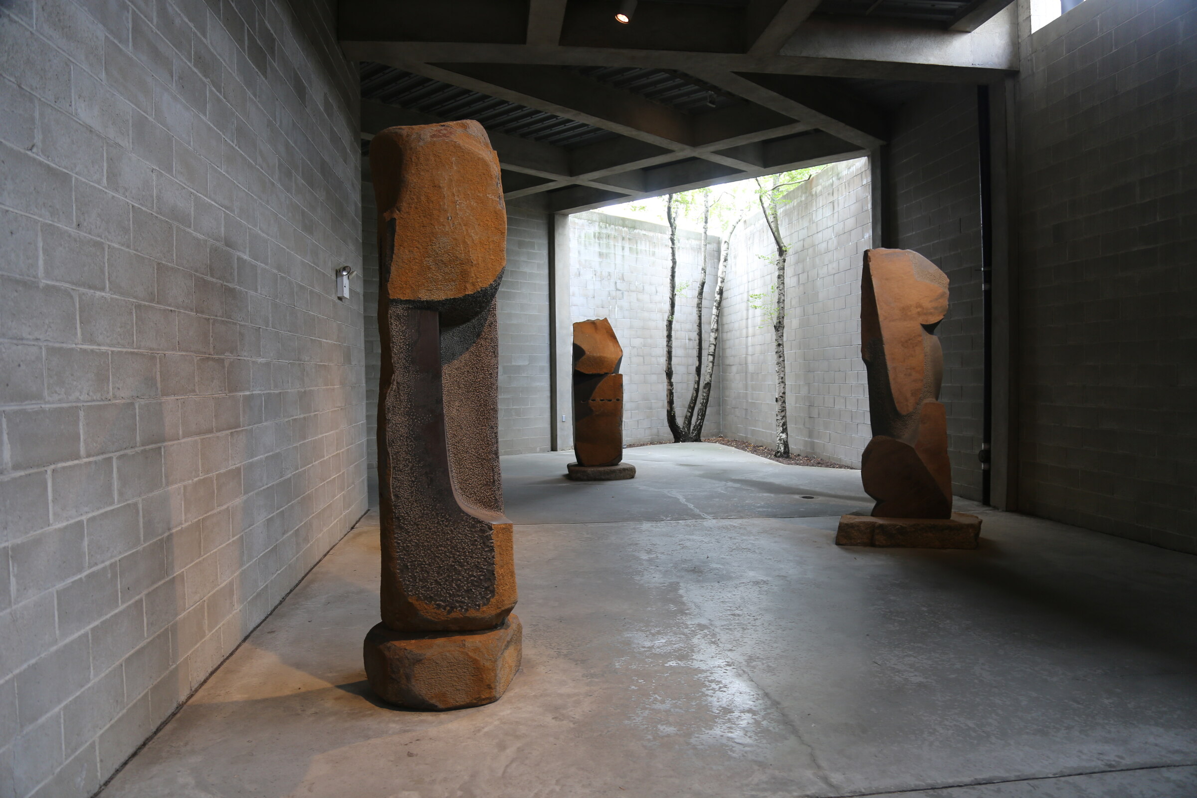 Long view through the To Bring to Life gallery toward carved stone sculptures and a courtyard