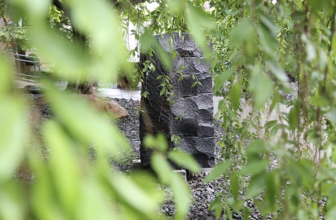 Dark stone sculpture glimpsed through the hanging branches of a willow tree