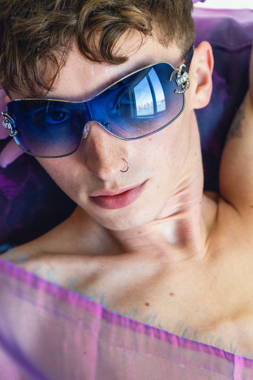 Ryder wearing blue glasses against violet fabric