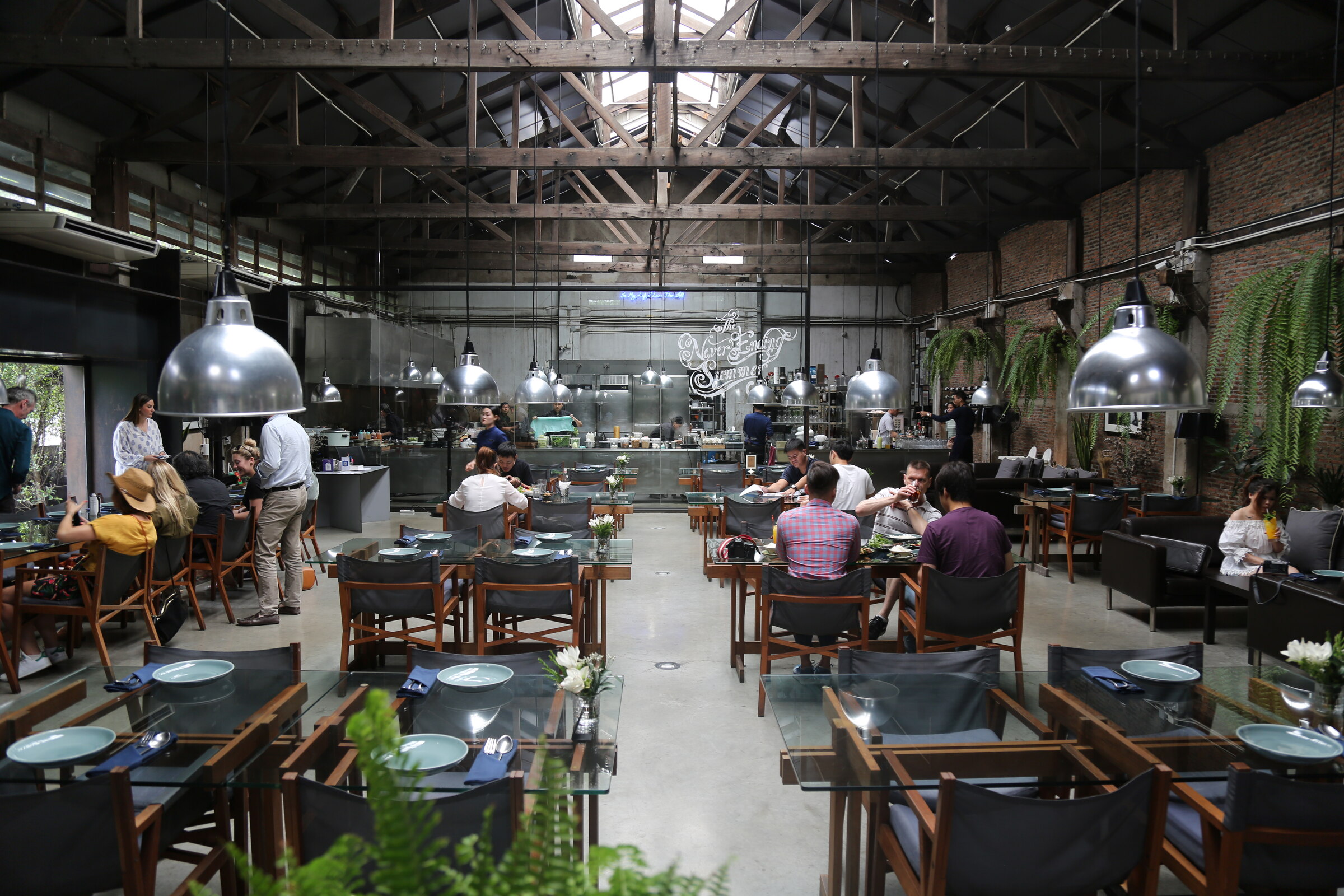 Industrial dining room with an open kitchen and suspended metal lights in Bangkok