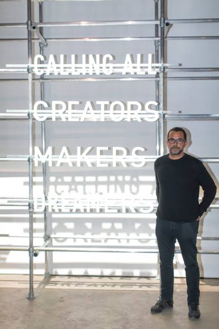 José Cabaço standing before a light installation reading Calling All Creators Makers