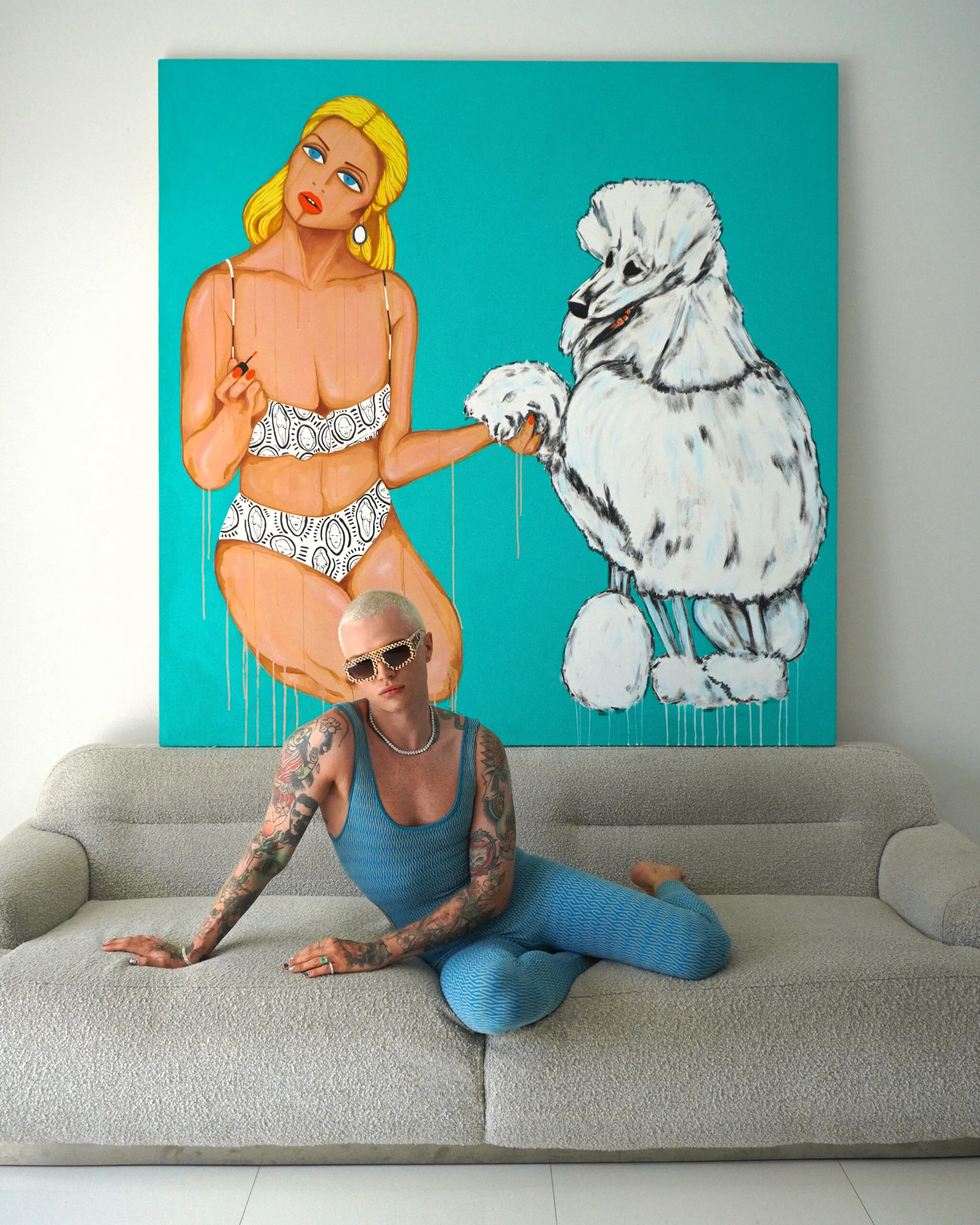 Patrick Church reclining on a white sofa beneath a painting of a woman and a white poodle